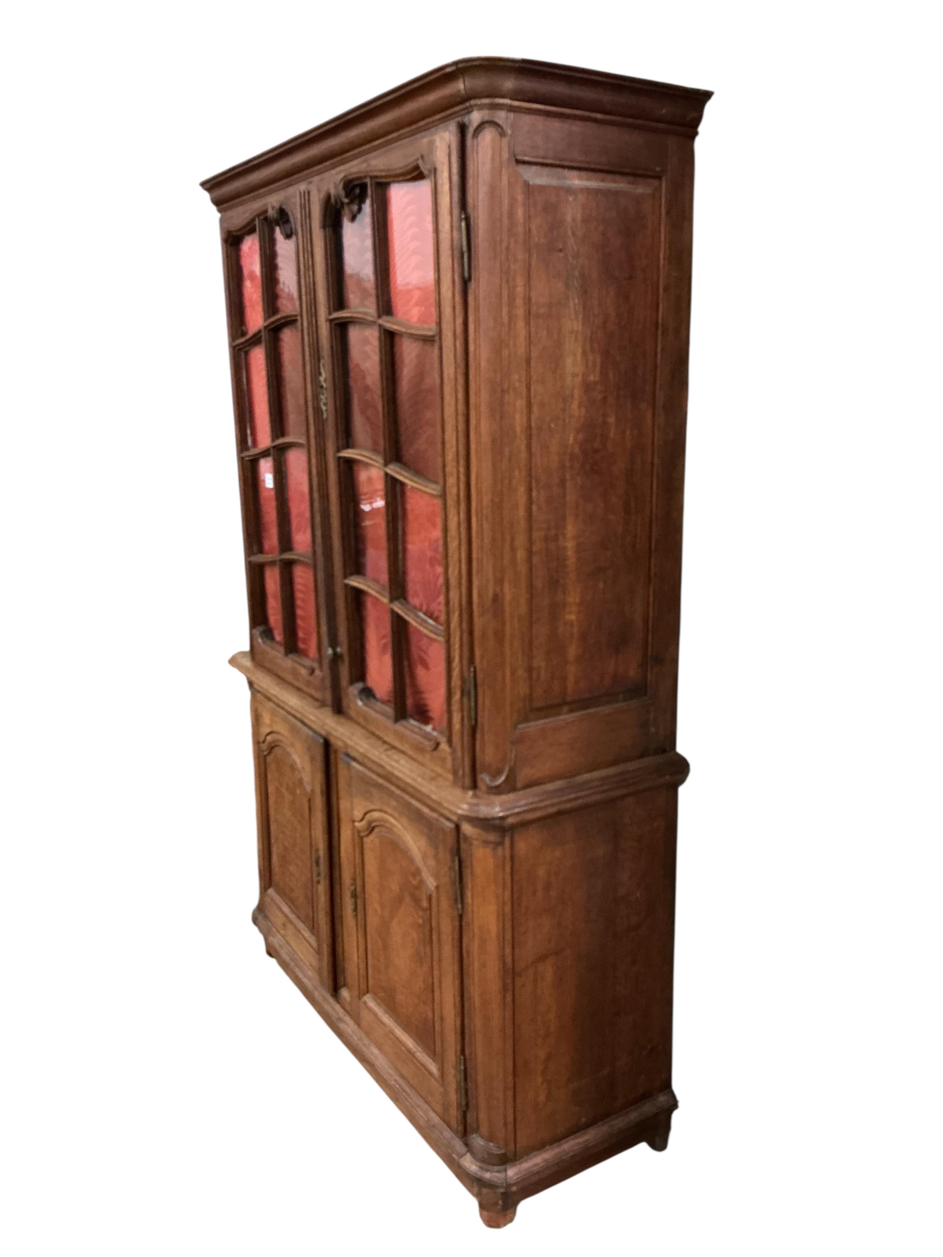 An early 19th century French Burgundian oak cabinet with two glazed doors over two arched panelled door, width 130cm, depth 49cm, height 206cm